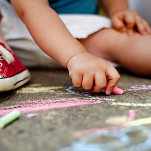 Close up of little boy in canvas shoes drawing with chalks on the sidewalk